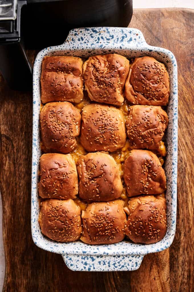 Twelve Air Fryer Big Mac Sliders with toasted sesame seed buns in a blue speckled baking dish, resting on a wooden board next to a black air fryer.