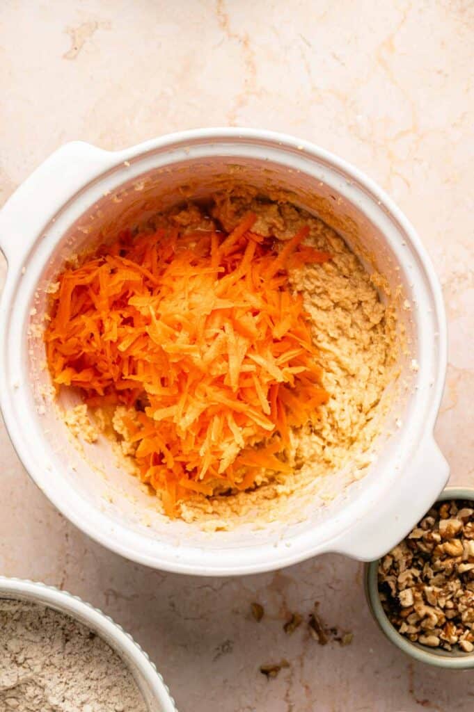 Fresh shredded carrots piled into cookie batter before mixing in for carrot cake cookies
