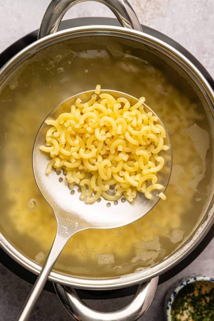 Slotted spoon lifting cooked cavatappi pasta out of a pot of boiling water