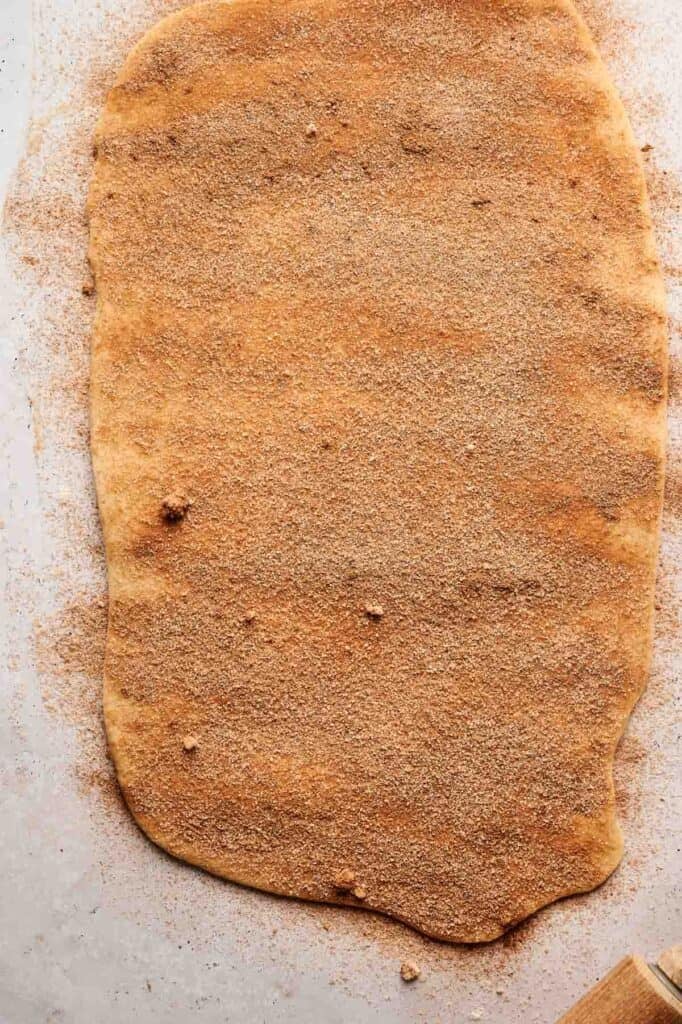 Rolled-out cinnamon swirl bread dough on a flat surface, evenly coated with a cinnamon sugar mixture.