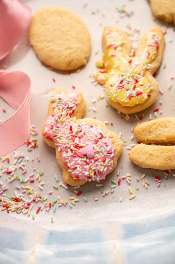 Pastel-iced bunny cookies with rainbow sprinkles next to plain baked cookies