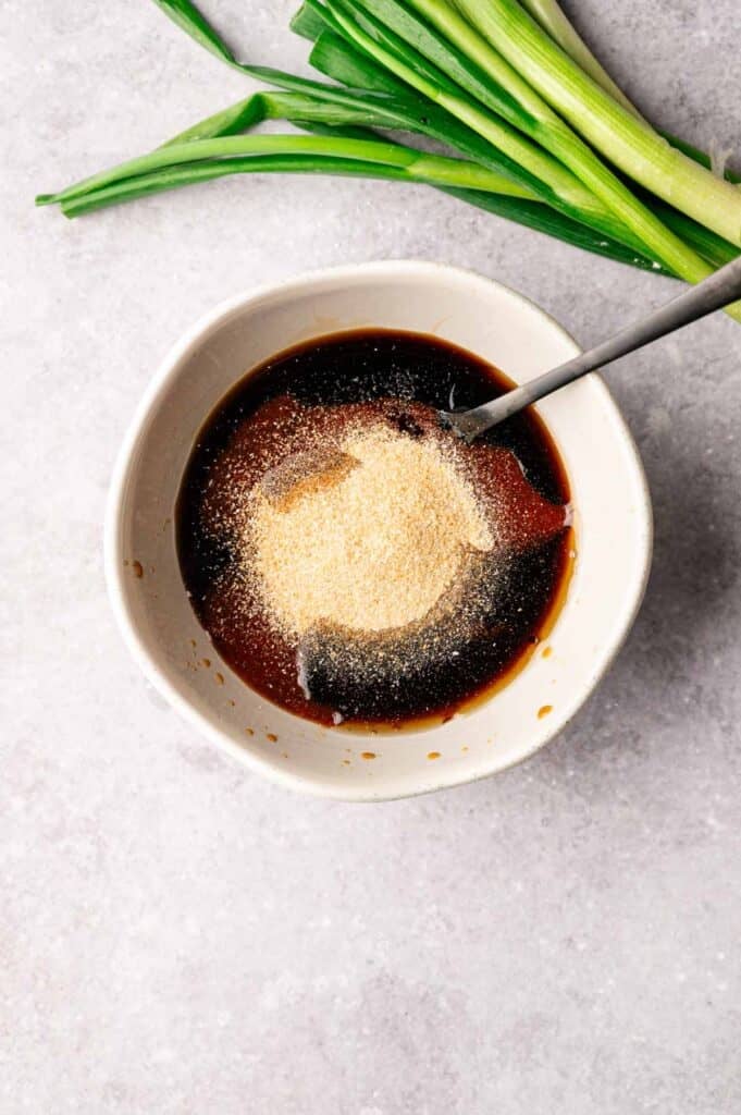 Soy sauce, garlic powder, and seasonings in a bowl with green onions nearby