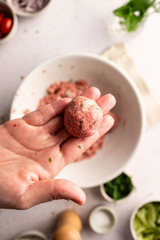 Hand rolling lamb mixture into a meatball over the mixing bowl