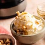 A bowl of Ninja Creami frozen yogurt topped with honey and chopped walnuts, served in a grey ceramic bowl with a side of walnuts and a Ninja Creami machine in the background.