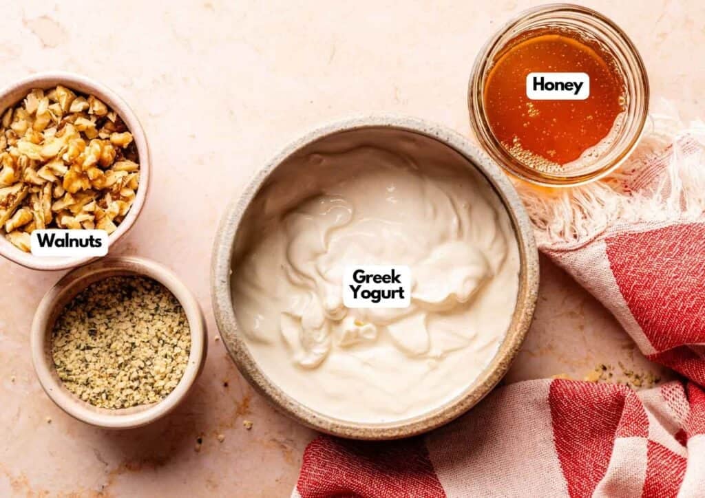Two bowls of Ninja Creami frozen yogurt topped with granola and honey, served on a grey surface with a whole mango, a half pineapple, and a small side bowl of extra granola.