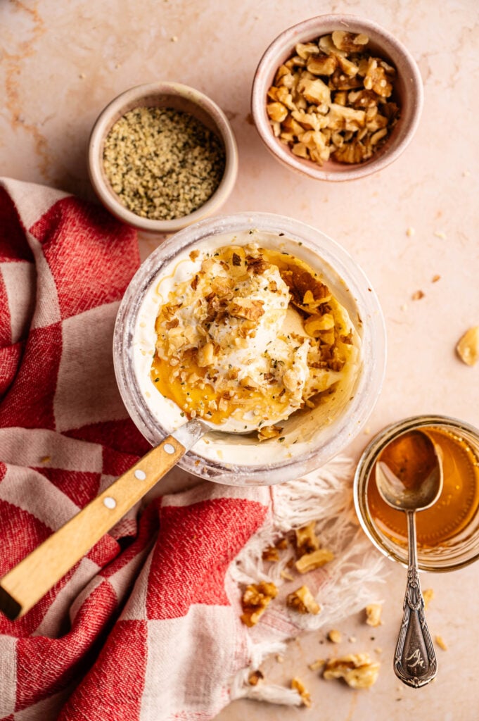 Ninja Creami frozen yogurt topped with honey drizzle, chopped walnuts, and hemp seeds, styled with a vintage spoon and red checkered linen.