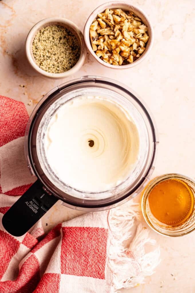 Ninja Creami pint container with frozen yogurt base ready to process, surrounded by hemp seeds, chopped walnuts, and honey toppings.
