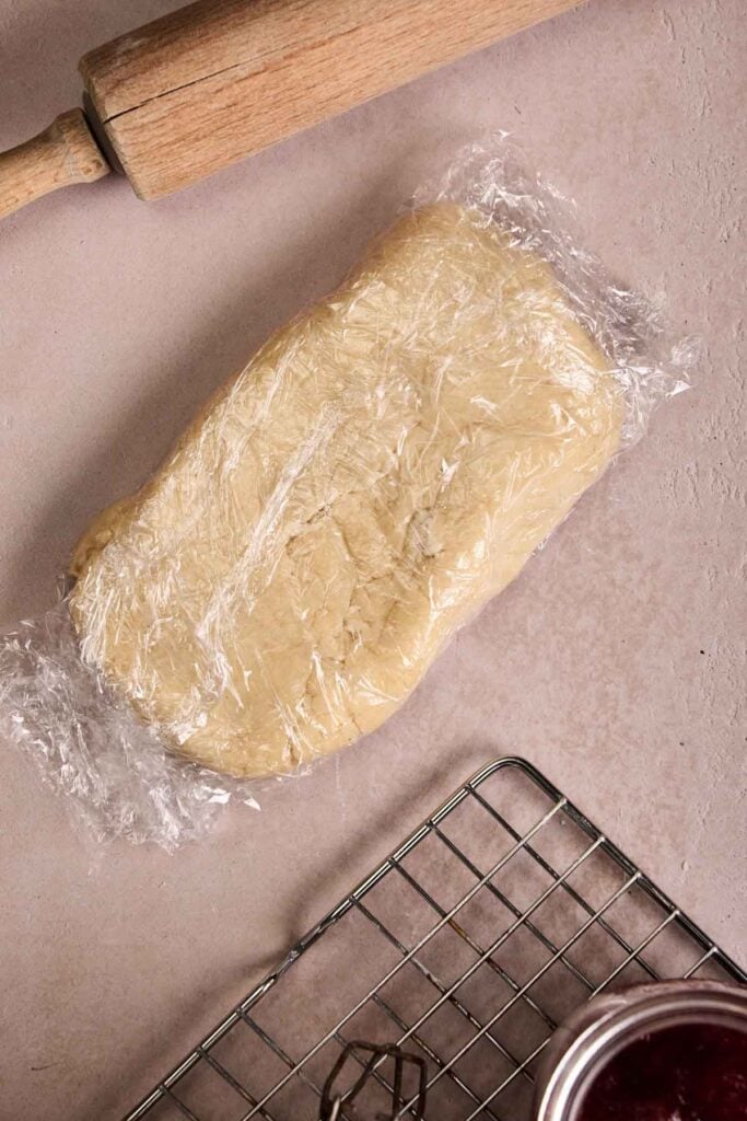 Chilled sourdough pastry dough wrapped in plastic next to a rolling pin