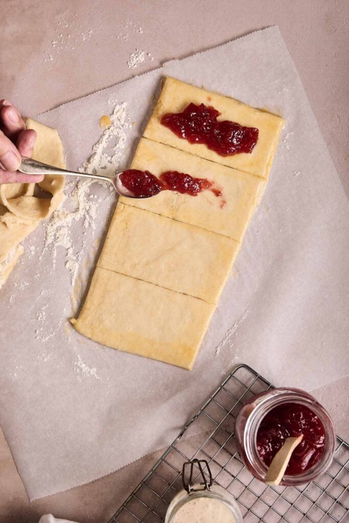Hand spreading jam over a rectangle of dough cut into strips for pop tarts