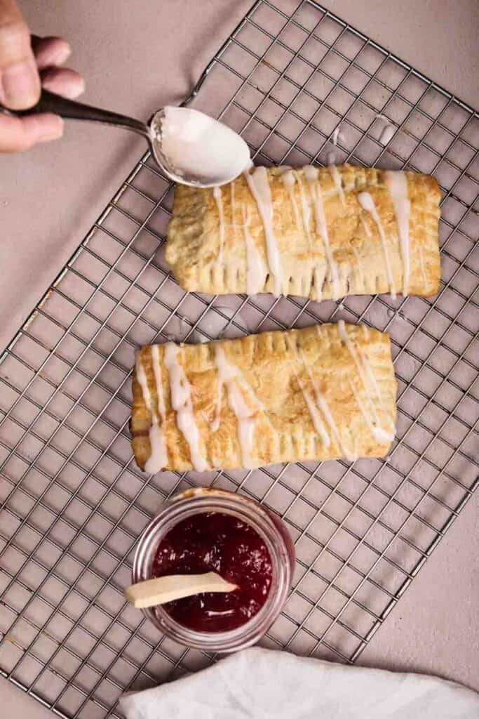 Golden baked pop tarts on a cooling rack being drizzled with white glaze