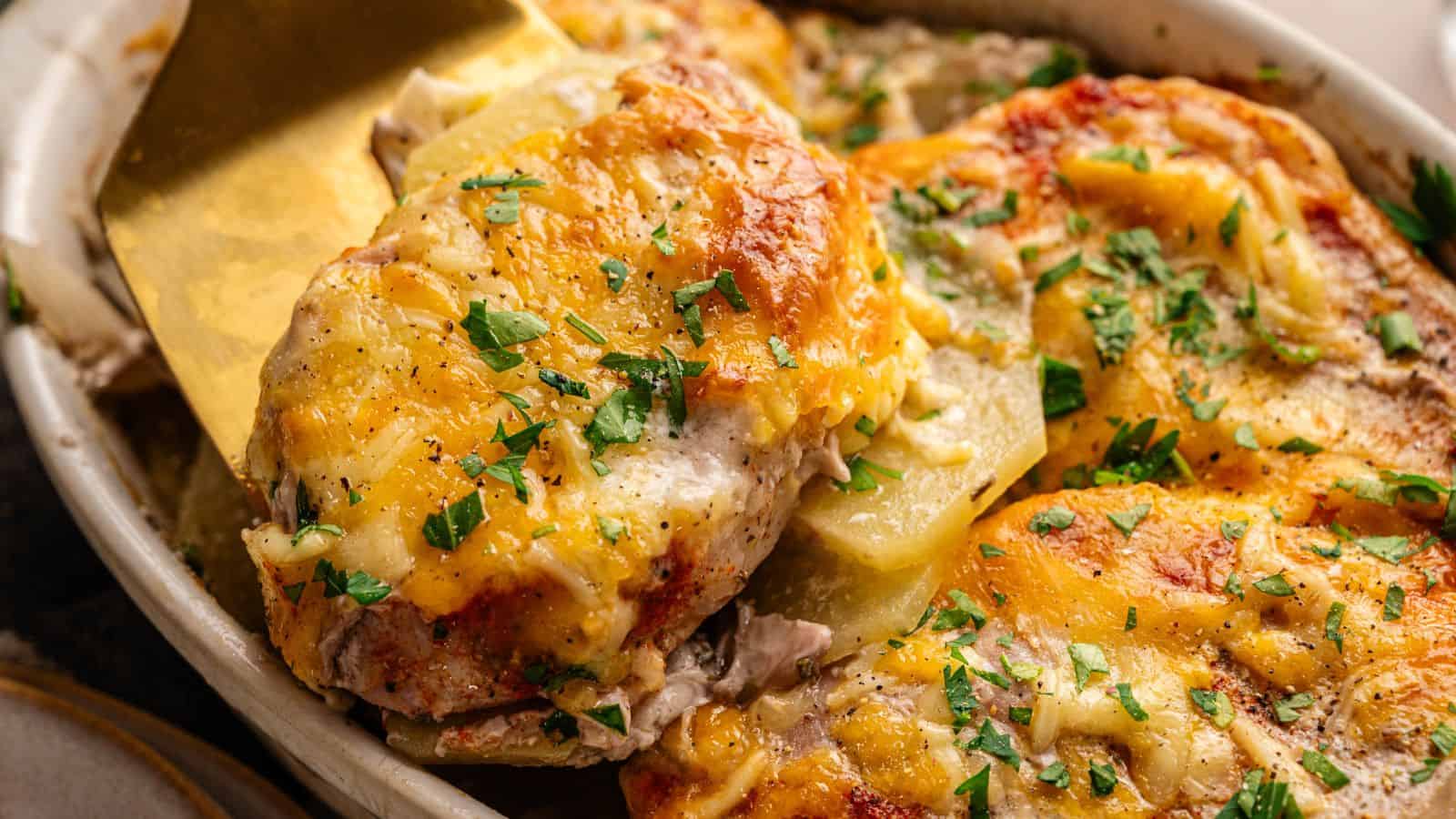 A close-up of a cheesy baked chicken casserole topped with chopped parsley, being served with a spatula.