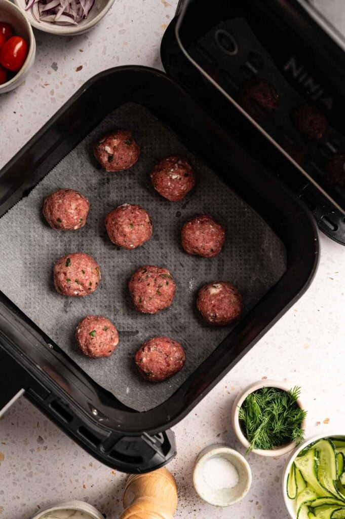 Raw lamb meatballs in a single layer in a Ninja air fryer basket, ready to cook.