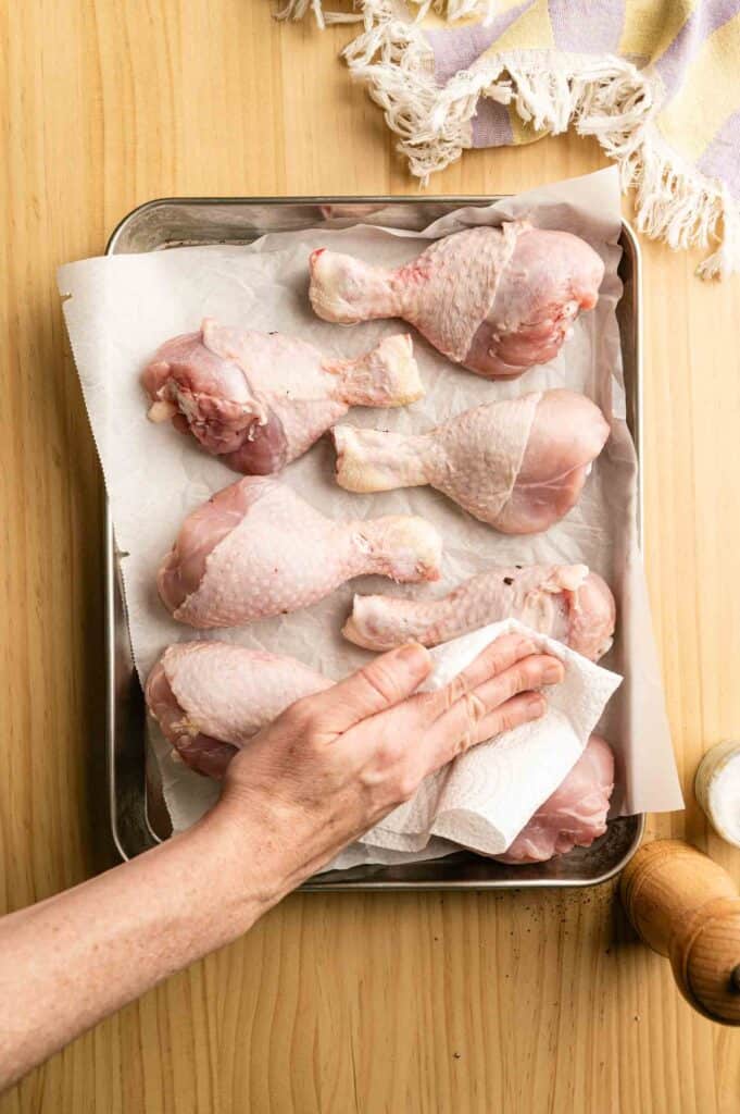 Hand drying chicken drumsticks on a baking sheet before oiling and seasoning
