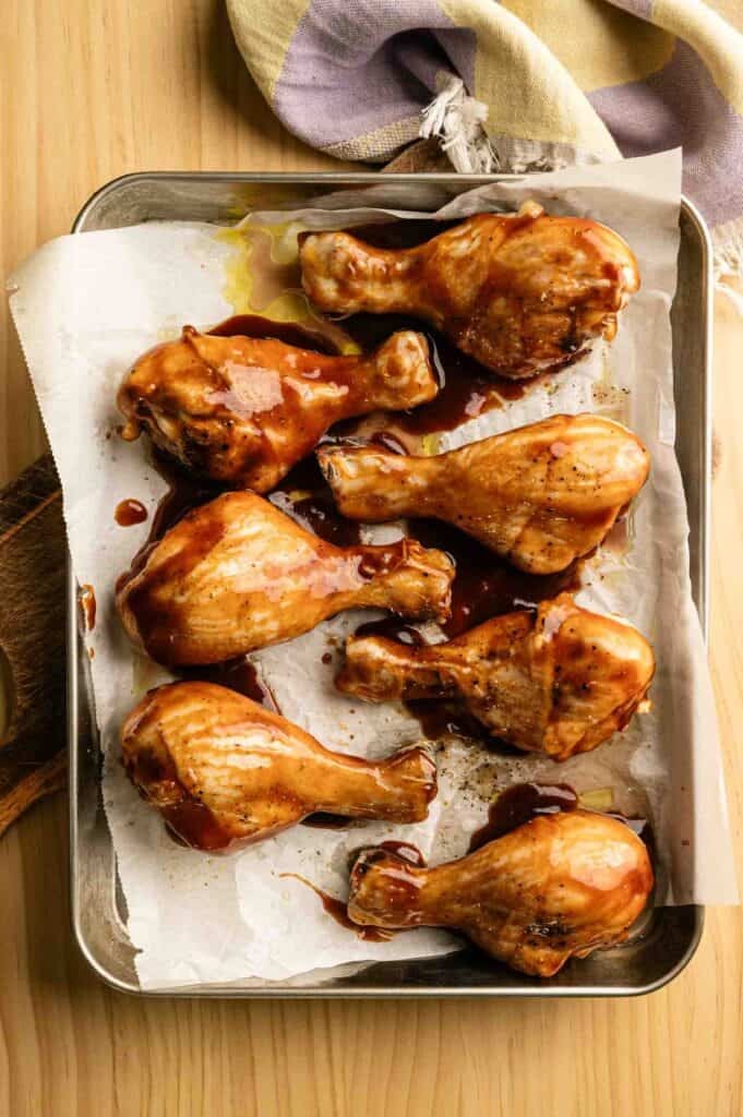 BBQ drumsticks with smoky glaze on a baking sheet.