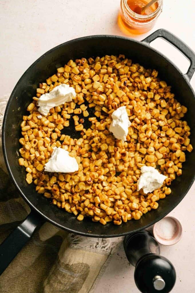 Cream cheese added in spoonfuls to buttery corn in a skillet