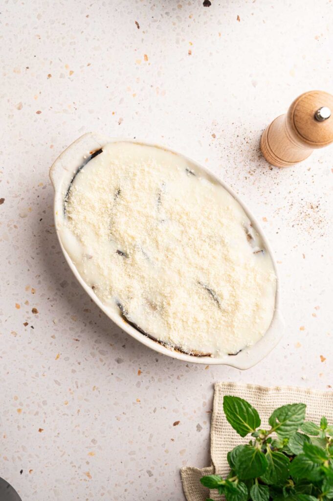 Unbaked moussaka in a casserole dish with creamy bechamel and cheese topping